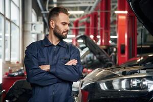 With, arms ,crossed, standing. Car repairman is in the garage with automobile photo