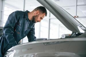 Side, view, hood is opened. Car repairman is in the garage with automobile photo