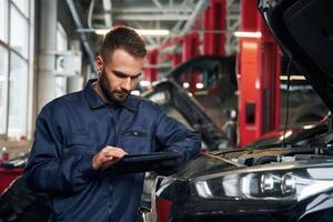 Using, tablet. Car, repairman is in the garage with automobile photo