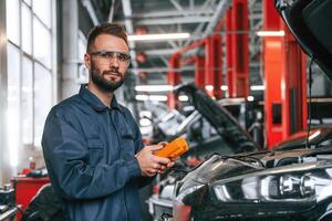Professional electro device in hands... Car repairman is in the garage with automobile photo
