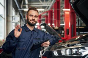 Using ,,tablet. Car repairman is in the garage with automobile photo