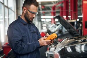 Checking electronics by ,,using device. Car repairman is in the garage with automobile photo