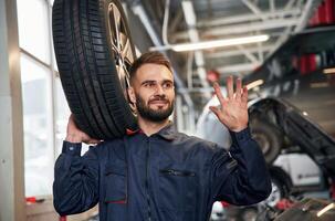 Holding, a ,tire. Car repairman is in the garage with automobile photo