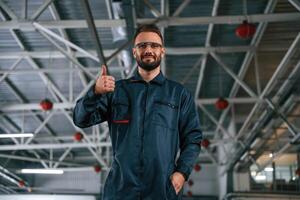 Standing, and posing,. Car repairman is in the garage with automobile photo