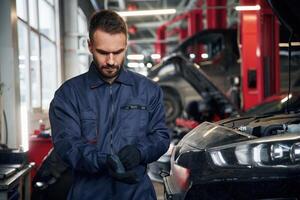 Wearing the, gloves, standing. Car repairman is in the garage with automobile photo