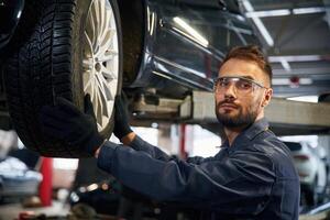 Looking, at ,the camera. Car repairman is in the garage with automobile photo