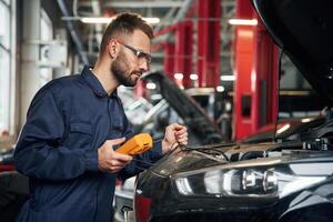 Checking, electronics by using device. Car repairman is in the garage with automobile photo