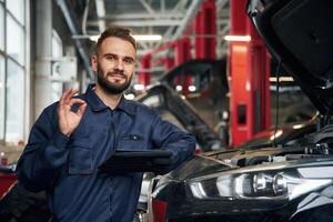 Using, tablet. Car repairman is in the garage with automobile photo