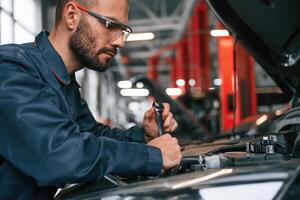 Hood is ,opened, fixing. Car repairman is in the garage with automobile photo