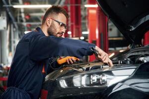 Professional, electro ,device in hands. Car repairman is in the garage with automobile photo