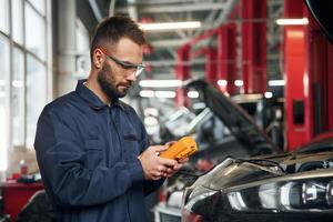 Professional ,electro device in hands. Car repairman is in the garage with automobile photo