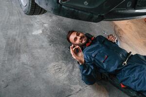 On, the,, ground with tool. Car repairman is in the garage with automobile photo