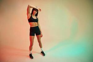 Standing, and doing exercises. Young woman in fitness clothes is in the studio photo
