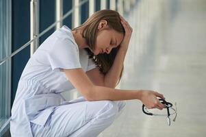 Sitting, taking a break, tired. Female doctor in white coat is in the hall photo