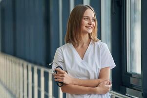 Standing, with arms crossed. Female, doctor in white coat is in the hall photo