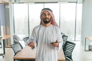 With smartphone in hand., Successful Muslim businessman in traditional outfit in his office photo
