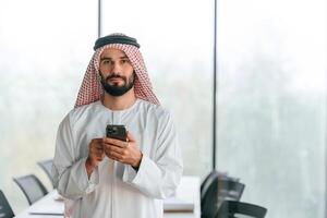With, smartphone ,in ,hand. Successful Muslim businessman in traditional outfit in his office photo