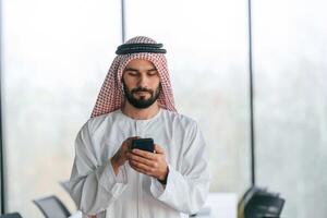 With smartphone in ,hand. ,,Successful Muslim businessman in traditional outfit in his office photo