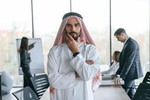 Standing in front of people that, behind... Muslim businessman in traditional outfit with colleagues in office photo