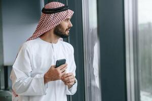 In the office with phone. Successful Muslim businessman in, traditional ,outfit photo