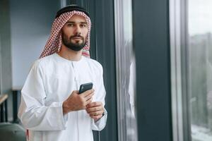 In the office with phone. Successful Muslim, businessman in, traditional outfit photo