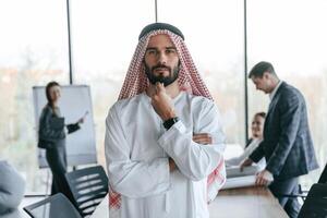 Standing in front of people that behind. Muslim businessman in traditional outfit with colleagues in office. photo