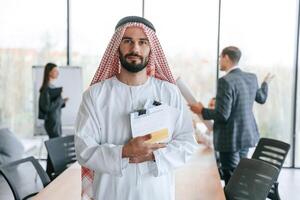 People behind Muslim businessman that is in traditional outfit with colleagues in ,,office photo