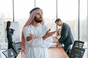 Standing in front, of, people that behind. Muslim businessman in traditional outfit with colleagues in office photo