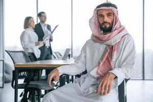 Serious, facial ,,expression. Muslim businessman in traditional outfit with colleagues in office photo