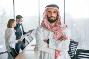 Front view., Muslim businessman in traditional outfit with colleagues in office photo