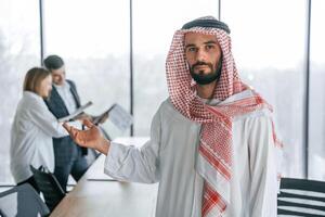 Looking at camera.,. Muslim businessman in traditional outfit with colleagues in office photo