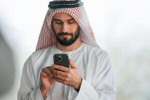 With ,smartphone in hand. Successful Muslim businessman in traditional outfit in his office photo