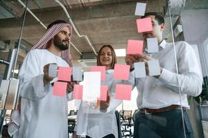 Using stickers, on the glass. Muslim businessman in traditional outfit with colleagues in office photo
