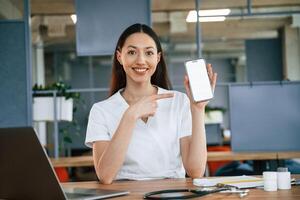 Holding smartphone ,with ,copy space on display. Female doctor in white coat is indoors photo