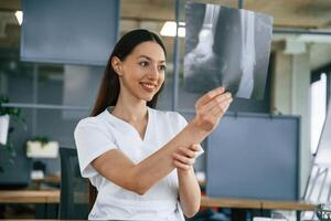 Looking, at x-ray. Female doctor in white coat is indoors photo