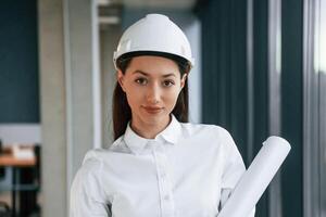 Portrait ,,of female architect that is in hard hat and in white clothes indoors photo