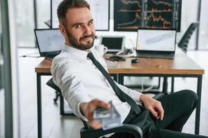 Giving lot of money.,. Holding in hand. Businessman is sitting by computer and working in the office photo