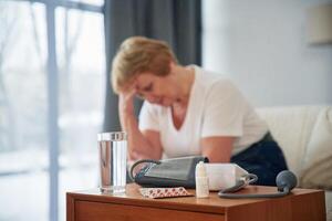 Sick, feeling bad. Pills on the table. Senior elderly woman is at home in the living room photo