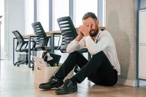 Depressed, sitting on the floor... Unemployed man is with personal belongings after being fired photo