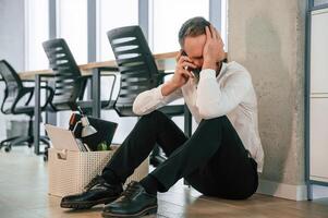 Depressed, sitting on the floor.,. Unemployed man is with personal belongings after being fired photo