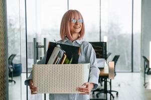 Standing and smiling,. Unemployed woman with pink hair is with personal belongings after being fired photo