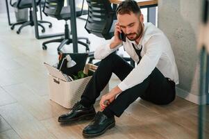 Depressed, sitting ,on, the floor,,. Unemployed man is with personal belongings after being fired photo