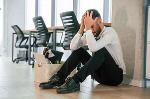Depressed, sitting ,on the floor. .Unemployed man is with personal belongings after being fired photo