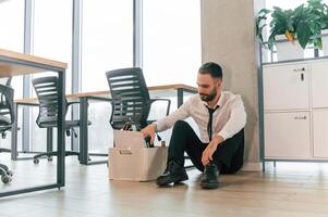 Feeling bad, sitting ,on floor. Unemployed man is with personal belongings after being fired photo