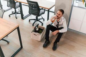 Feeling bad, sitting on, floor. Unemployed man is with personal belongings after being fired photo