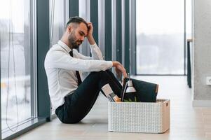 Feeling bad, sitting, on floor. Unemployed man is with personal belongings after being fired photo
