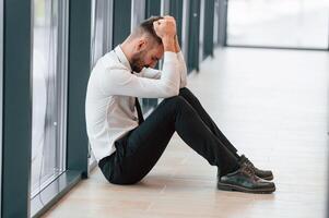 Depressive, office worker is sitting on the floor, side view photo