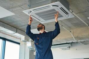 A man repairs the v,entilation system, the device hangs on the ceiling photo