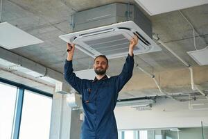 A ,man repairs the ventilation system, the device hangs on the ceiling photo