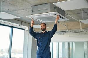 A man ,repairs the ventilation system, the device hangs on the ceiling photo